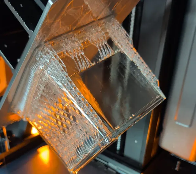 Pièce en résine transparente sur le plateau d'une imprimante 3D résine, encore sur ses supports